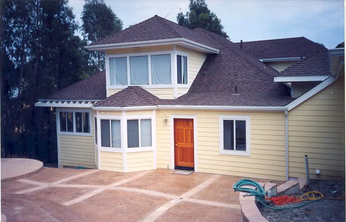Light yellow house with large windows, orange front door, and paved driveway