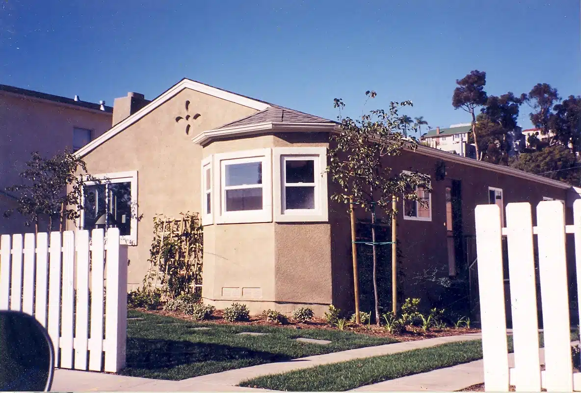 Small beige single-story home with bay window and landscaped front yard