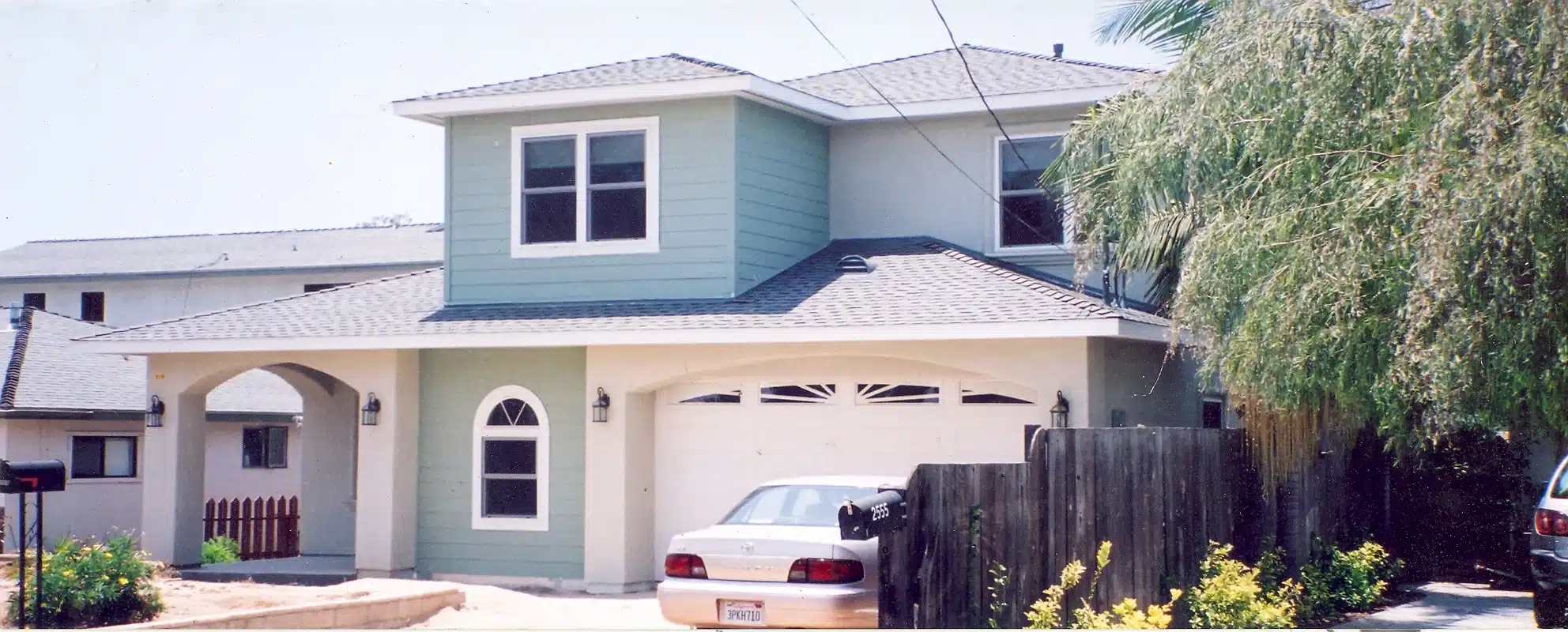 Two-story pastel green house with white trim, garage, and parked car in driveway